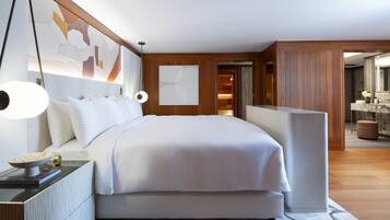 A modern bedroom with a large bed, bedside lamps, a nightstand, and a view into a bathroom.