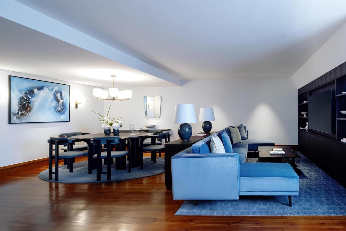 A modern living room with a blue sofa, a dining table with chairs, and a large abstract painting on the wall.