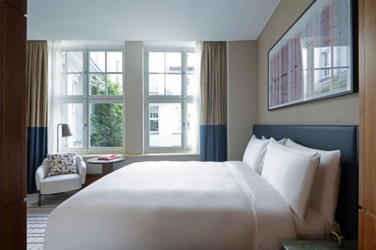 Ett hotellrum med en stor säng, en stol, ett litet bord och ett fönster med gardiner.
