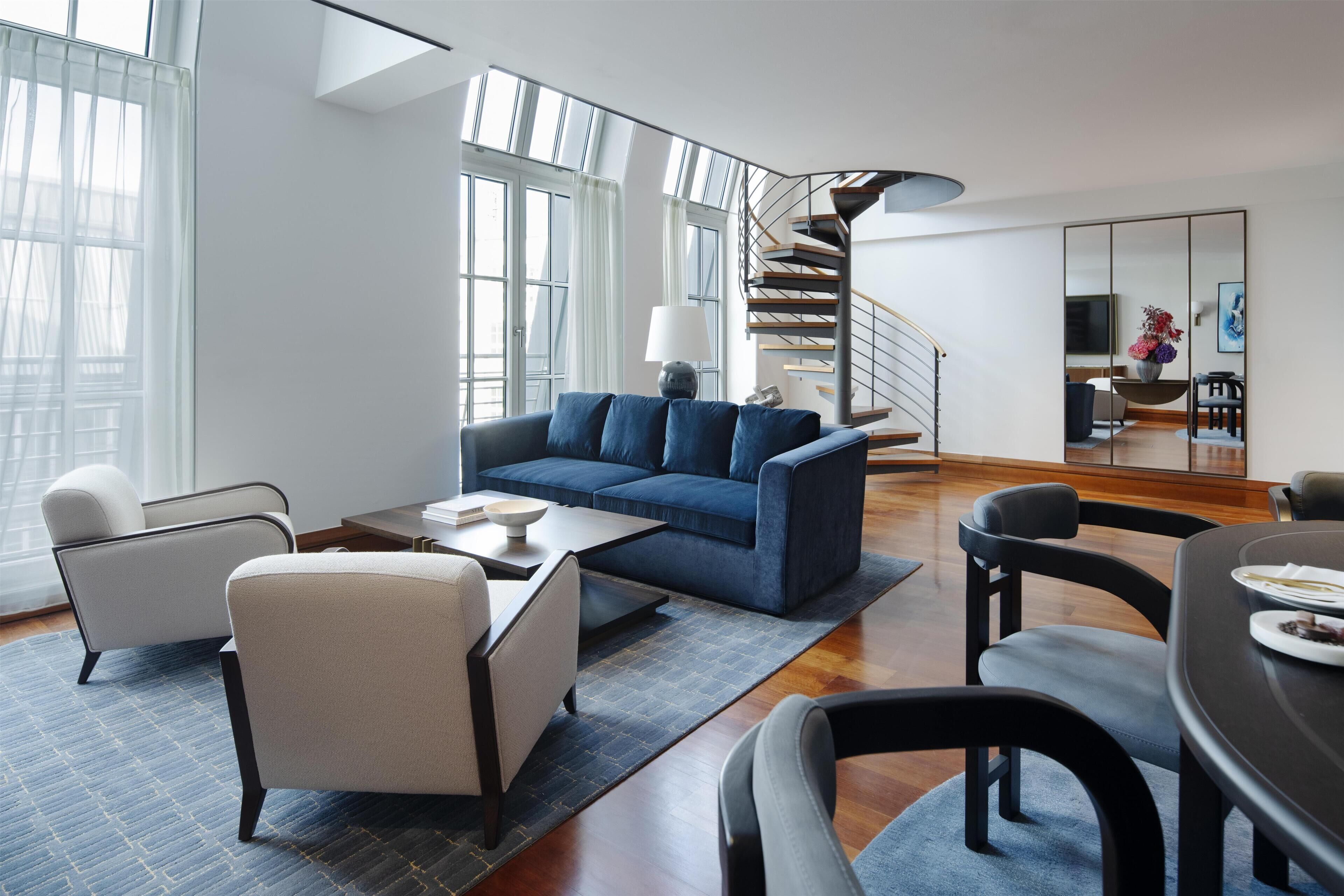 A modern living room with a blue sofa, a coffee table, and a dining area with a table and chairs.