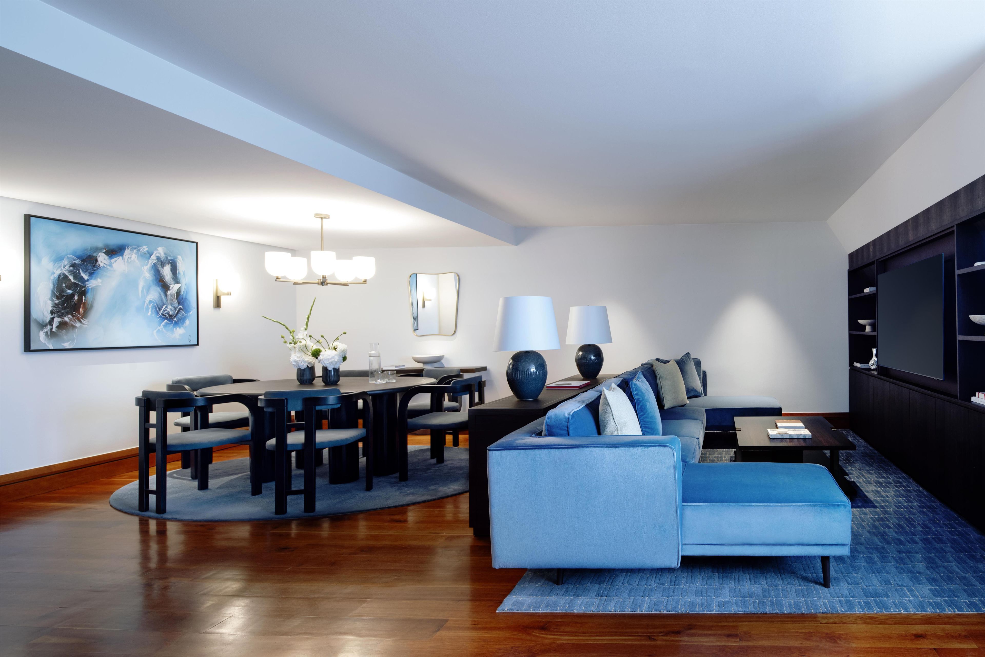 Een moderne woonkamer met een eethoek, met een bank, een salontafel, een eettafel met stoelen en een groot schilderij aan de muur.