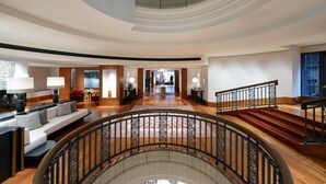 A spacious lobby with a curved staircase, a seating area with a sofa and lamps, and a view of the entrance. - Conrad Hamburg (Hamburg)
