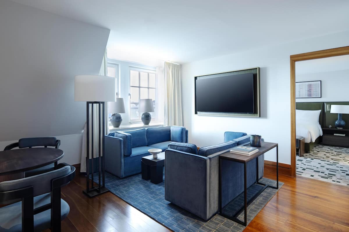 A modern living room with a blue sofa, a round dining table, and a flat-screen TV mounted on the wall.