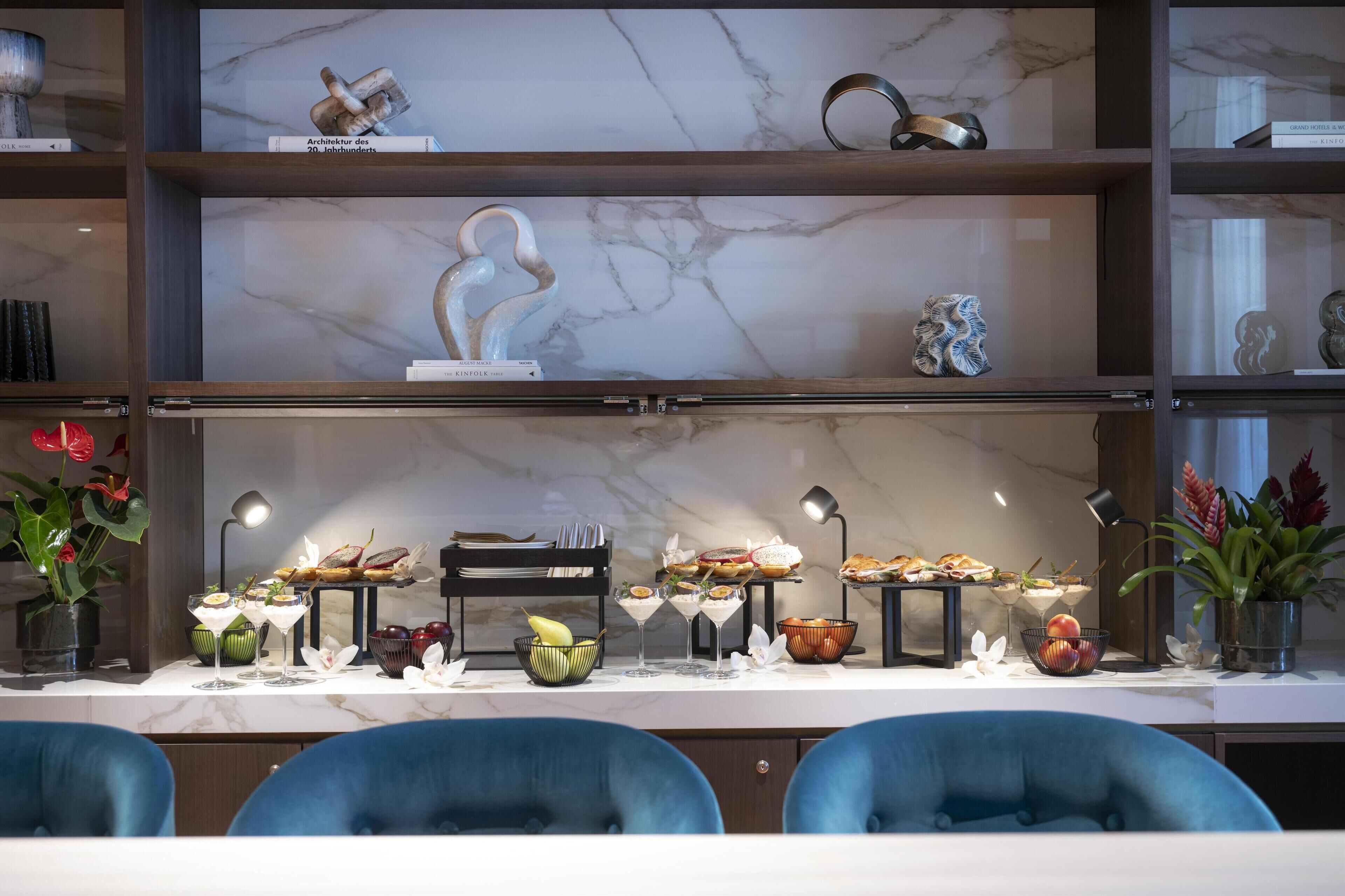 A modern dining area with marble countertops, blue chairs, and a variety of food and drink items displayed on the table.