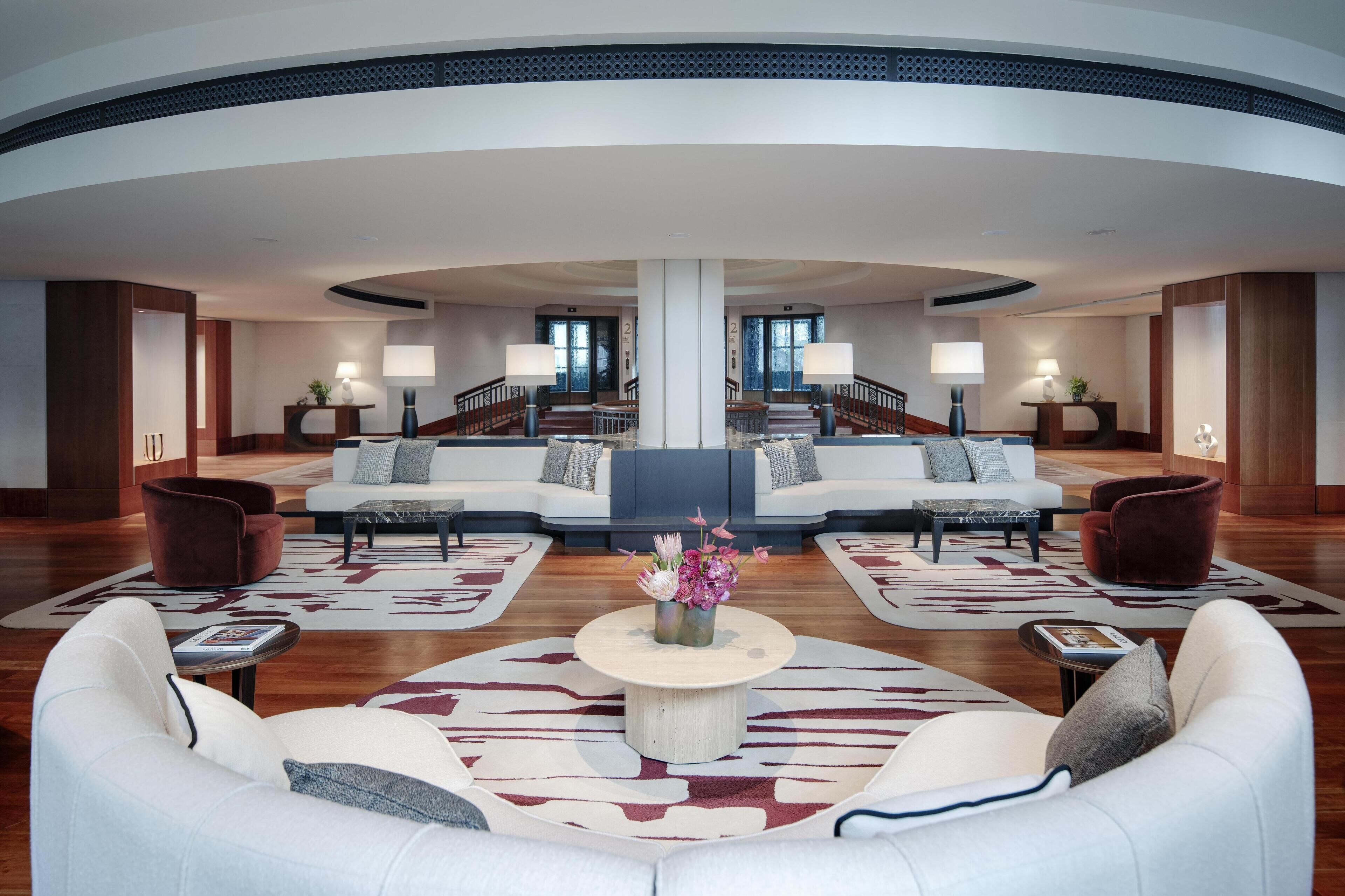 A spacious lobby with a central seating area, a staircase, and a view of the outside.