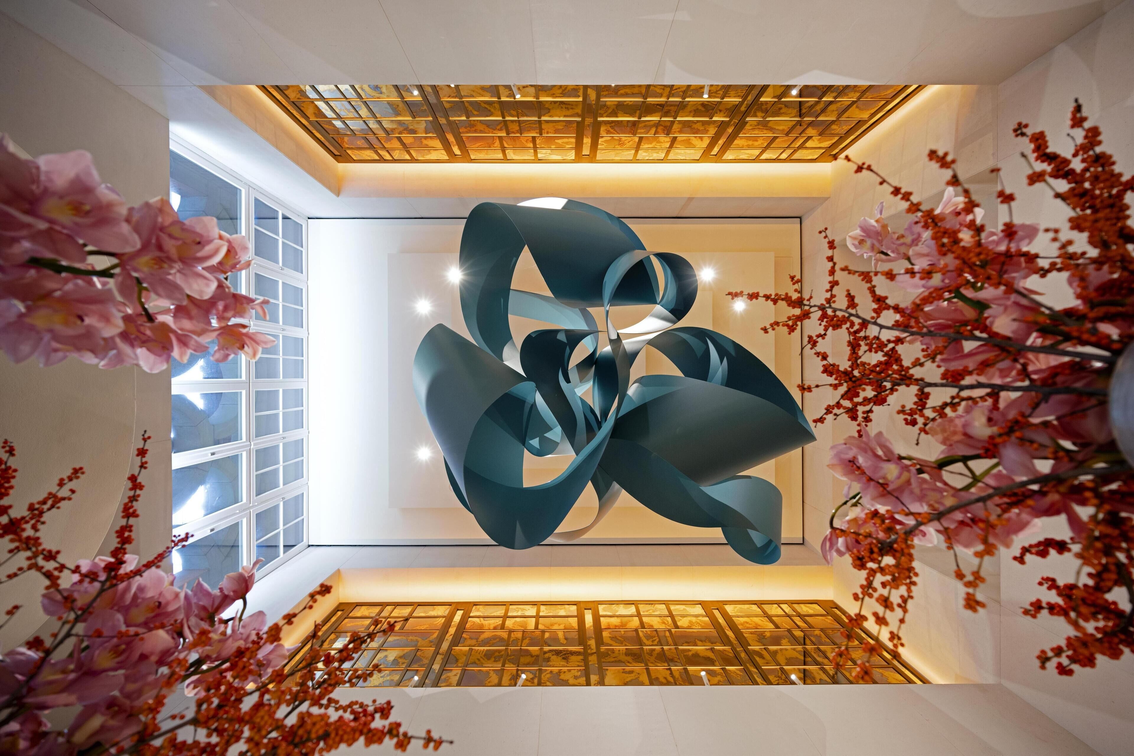 Un espacio interior con un diseño moderno en el techo, ventanas amplias y arreglos florales decorativos.