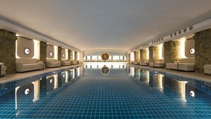 A large indoor swimming pool with a tiled floor, surrounded by seating areas and a central decorative feature. - Conrad Hamburg (Hamburg)