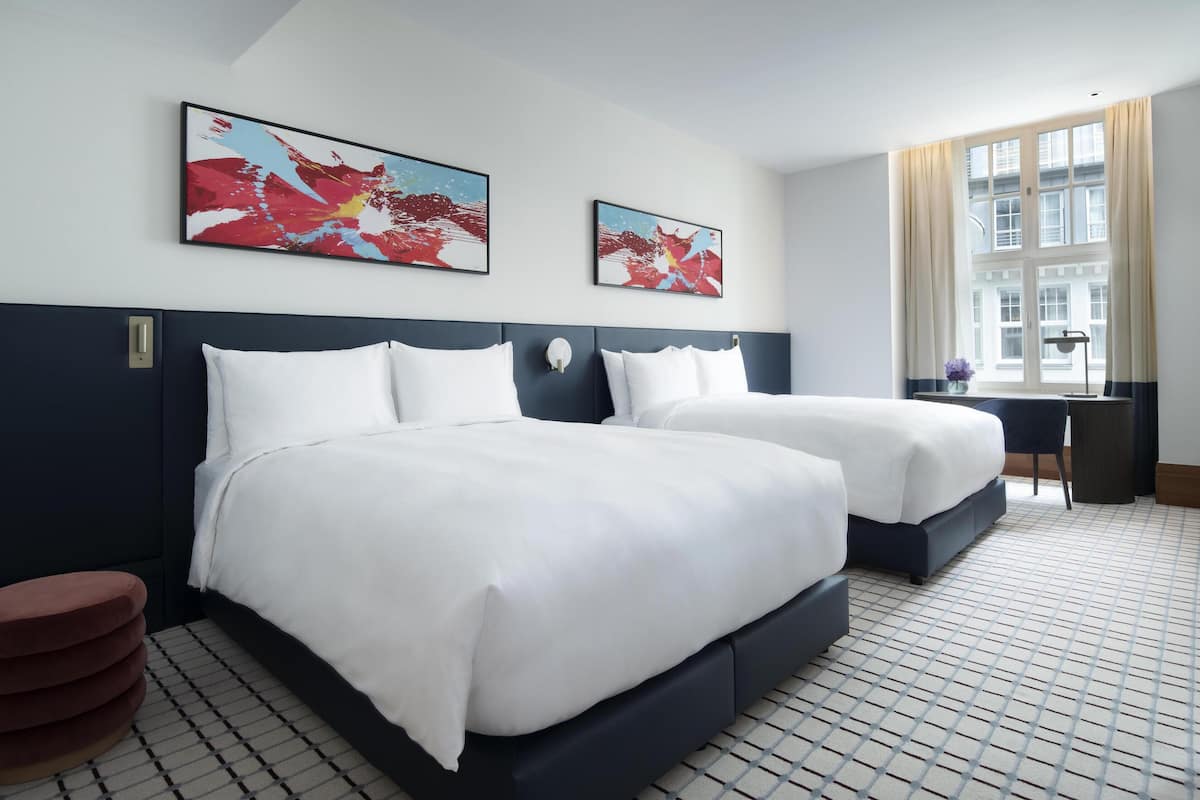 A hotel room with two beds, a desk, and a window with curtains.