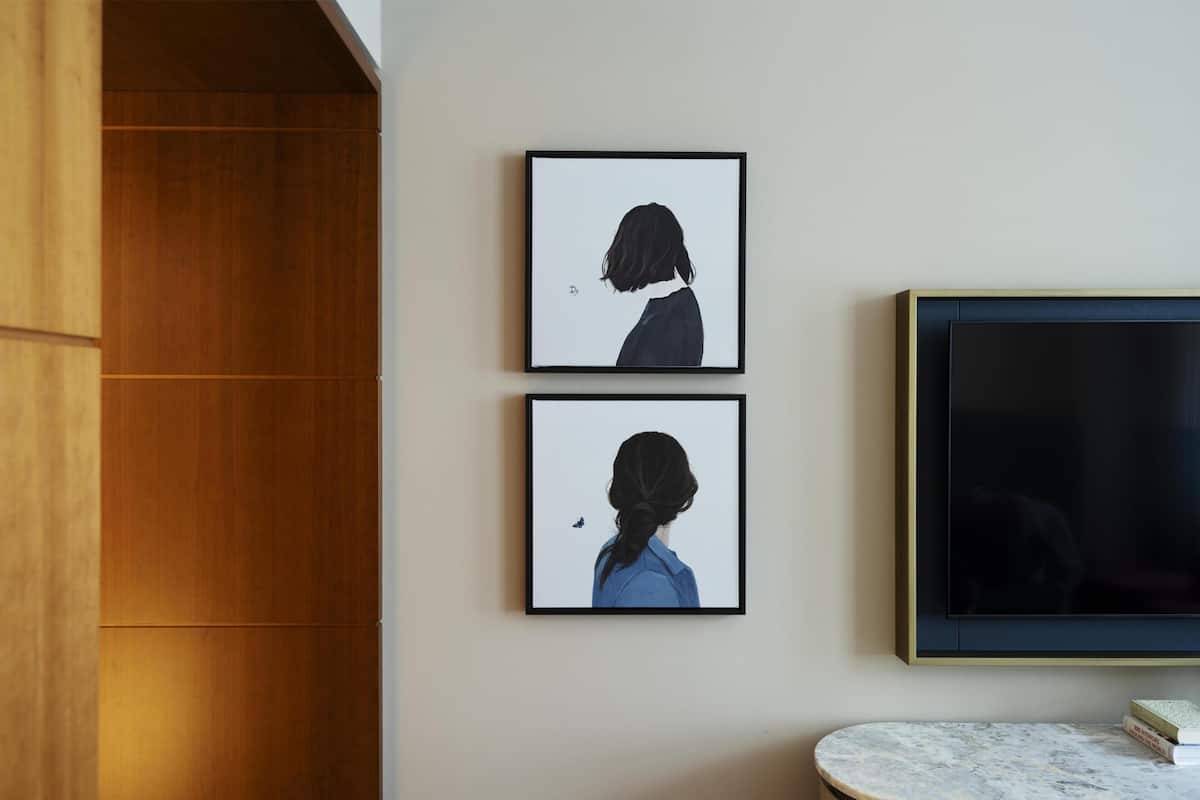 Two framed artworks on a wall, a flat-screen TV to the right, and a marble-topped table with books.