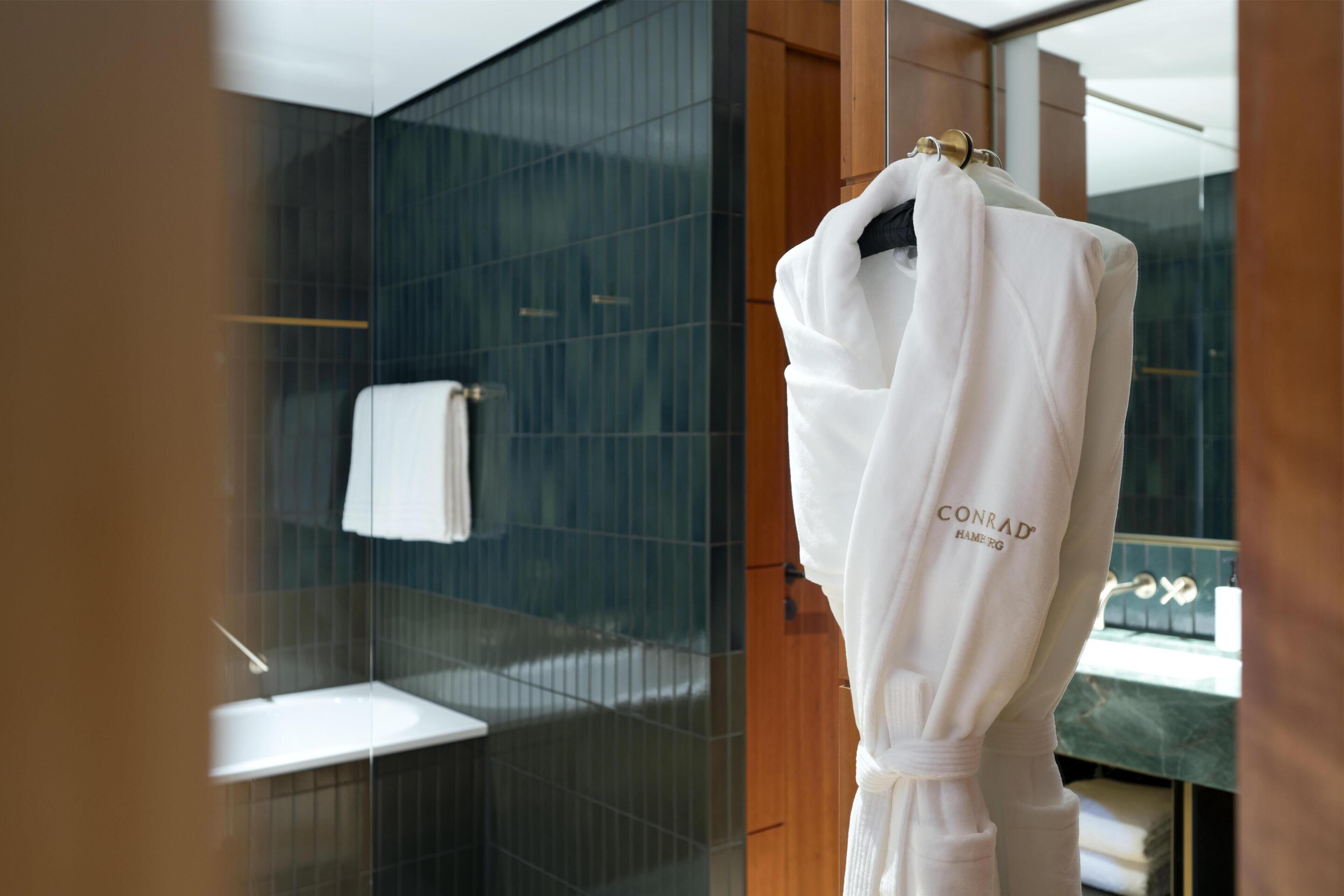 Une salle de bain d’hôtel avec une douche à parois de verre, un lavabo blanc et un peignoir suspendu à un porte-serviettes.