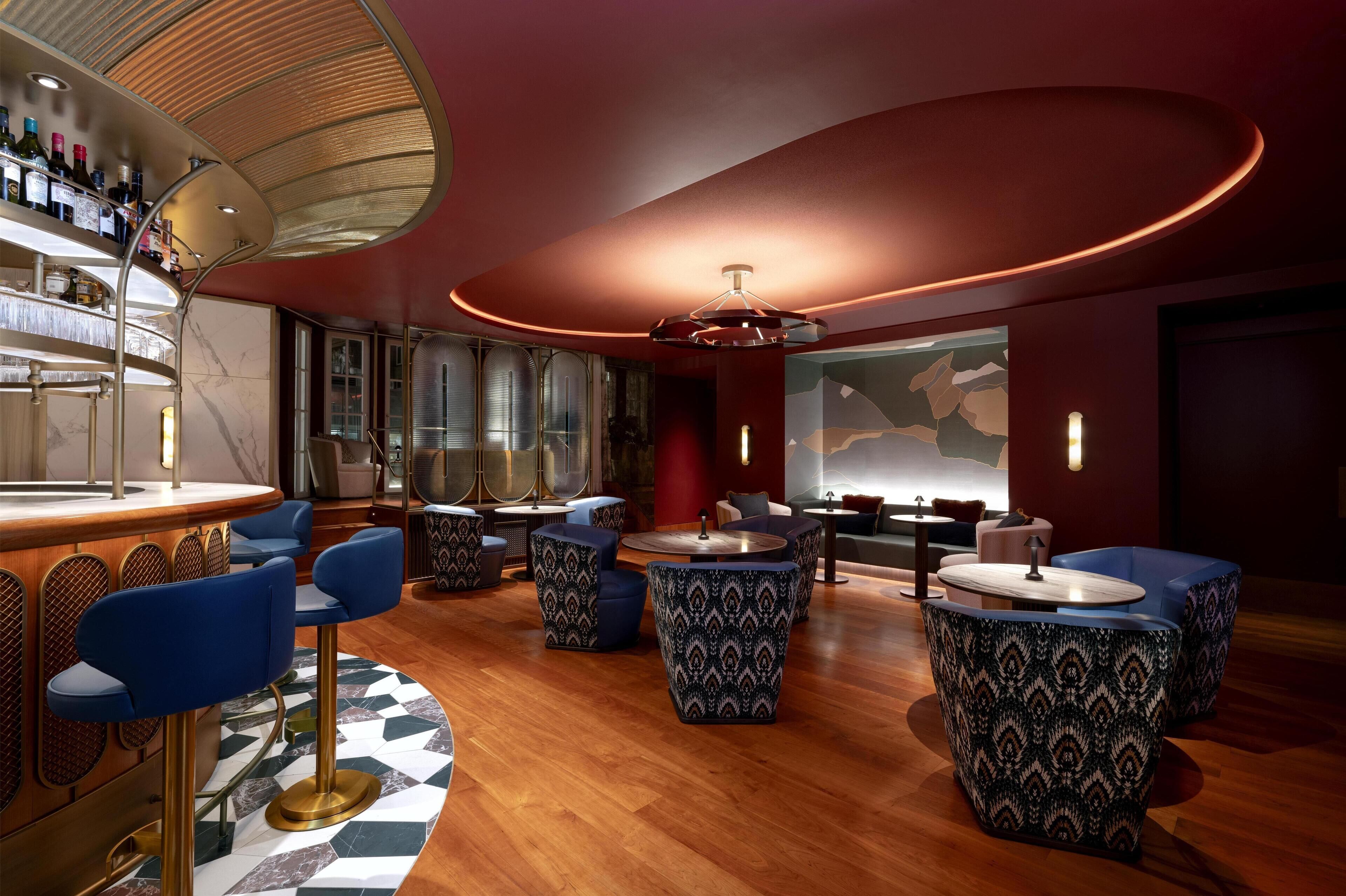 A modern bar area with blue bar stools, patterned round tables, and a wine display.