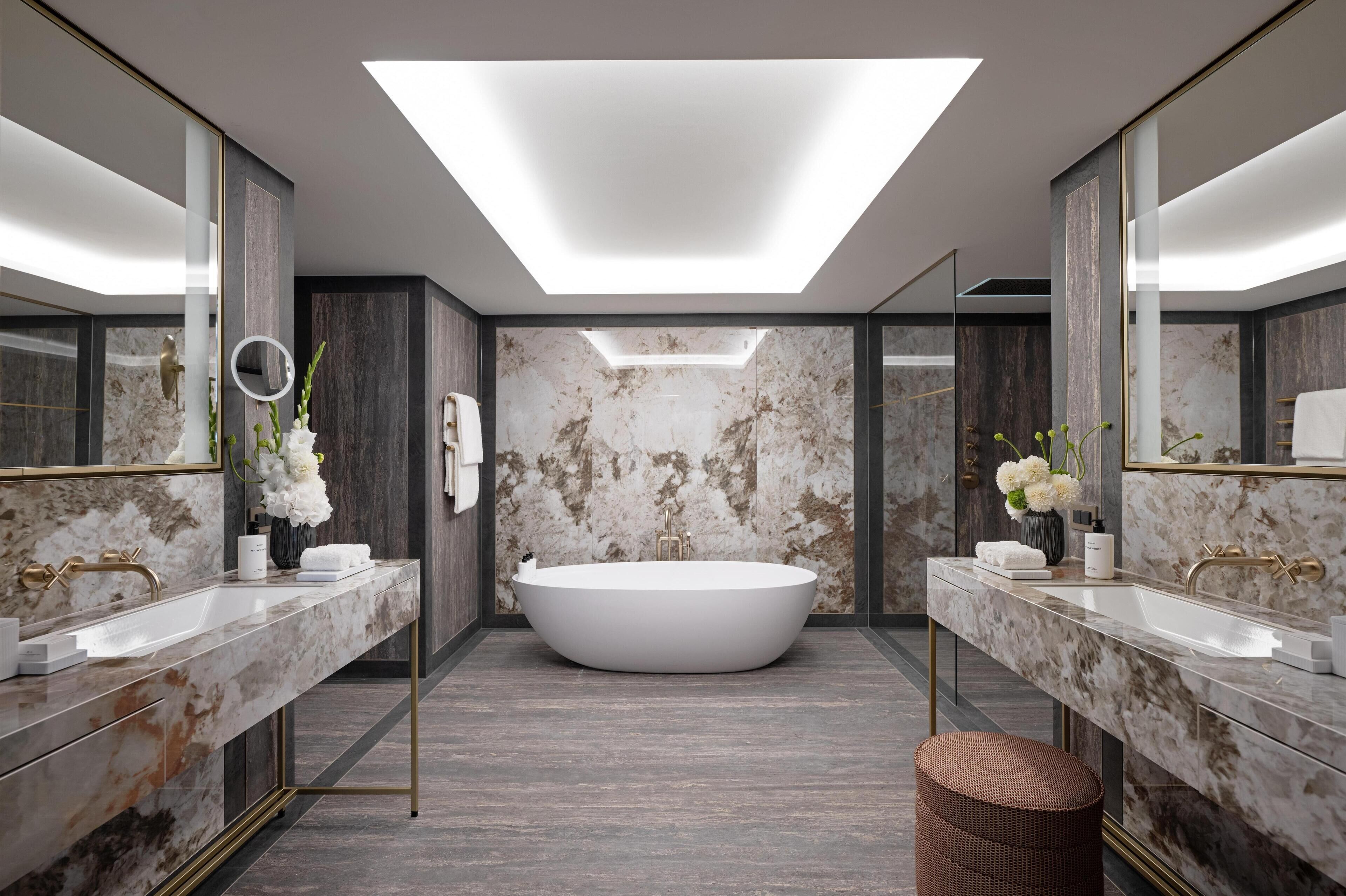 A modern bathroom with a freestanding bathtub, two sinks, marble countertops, and large mirrors.