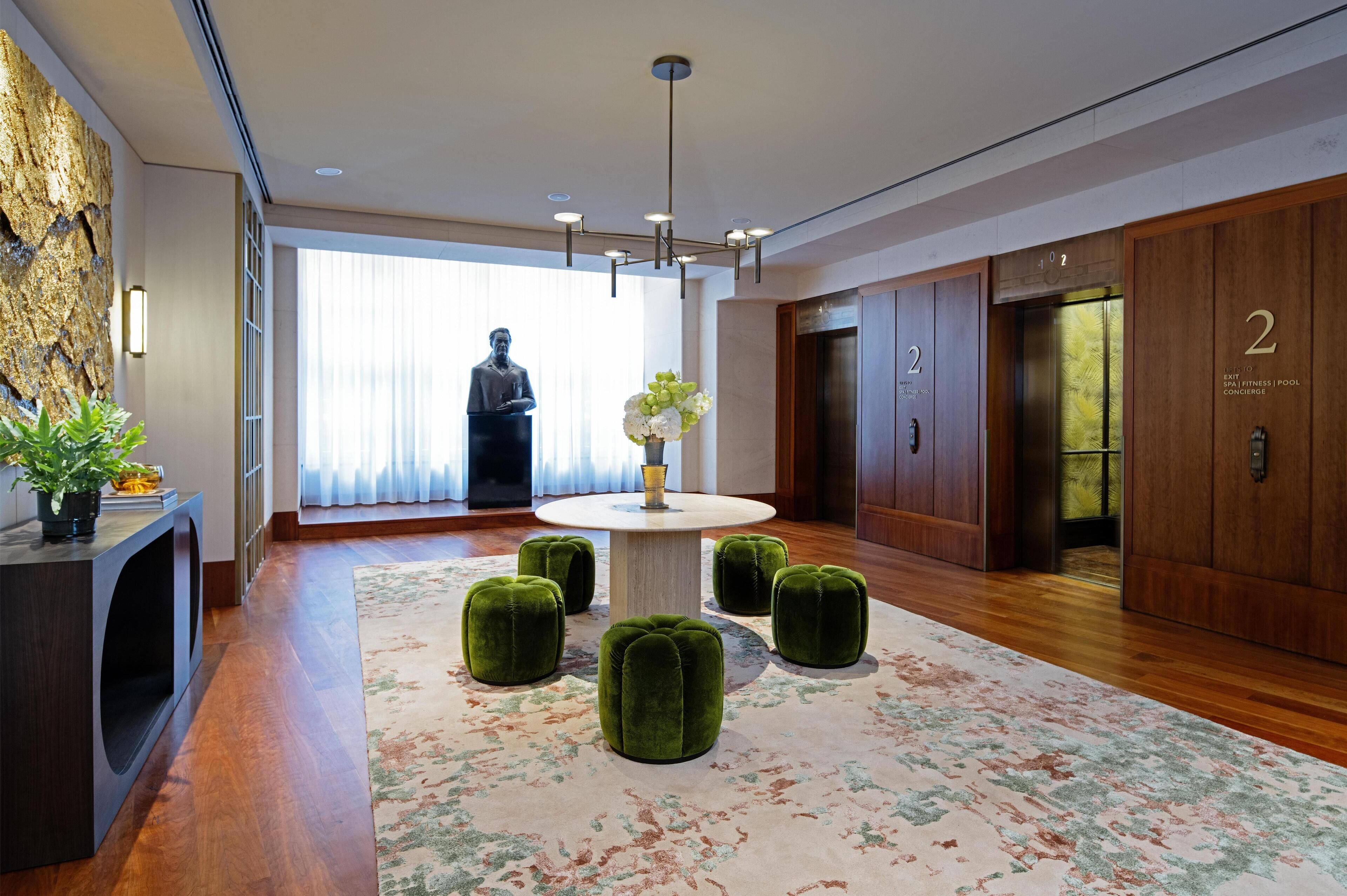 A modern lobby with a round table, green ottomans, a statue, and an elevator.