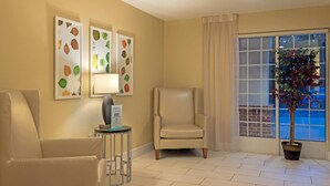 A room with a beige armchair, a smaller chair, a table with a lamp, and wall art depicting leaves. - MainStay Suites Raleigh - Cary (Cary)