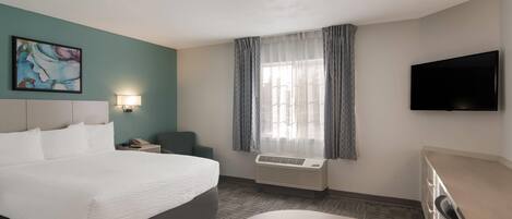 A hotel room with a large bed, a desk, a chair, a flat-screen TV, a window with curtains, and an air conditioning unit.