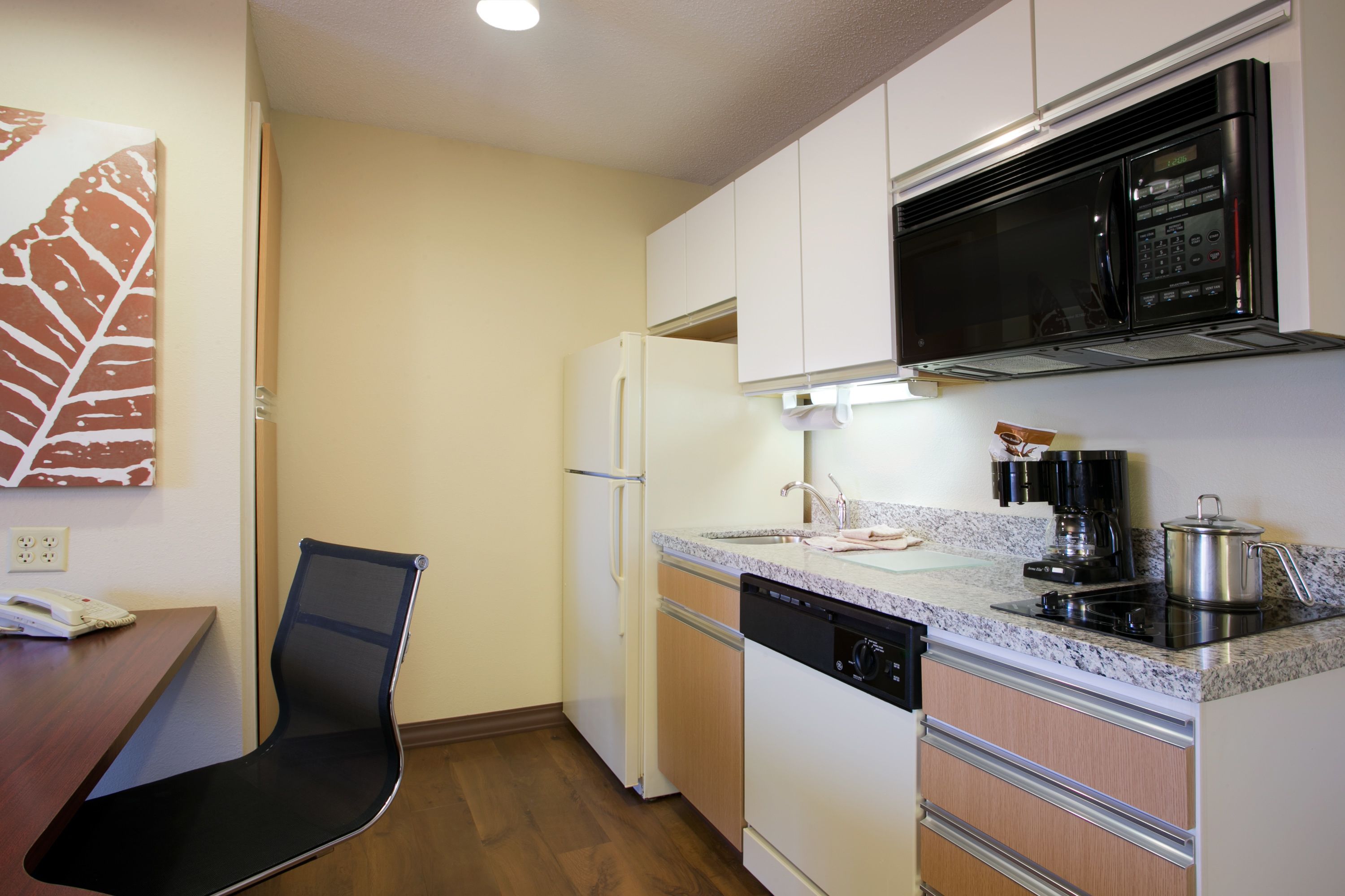 A compact kitchen with white cabinets, a black microwave, a dishwasher, and a wooden dining table with a black chair.
