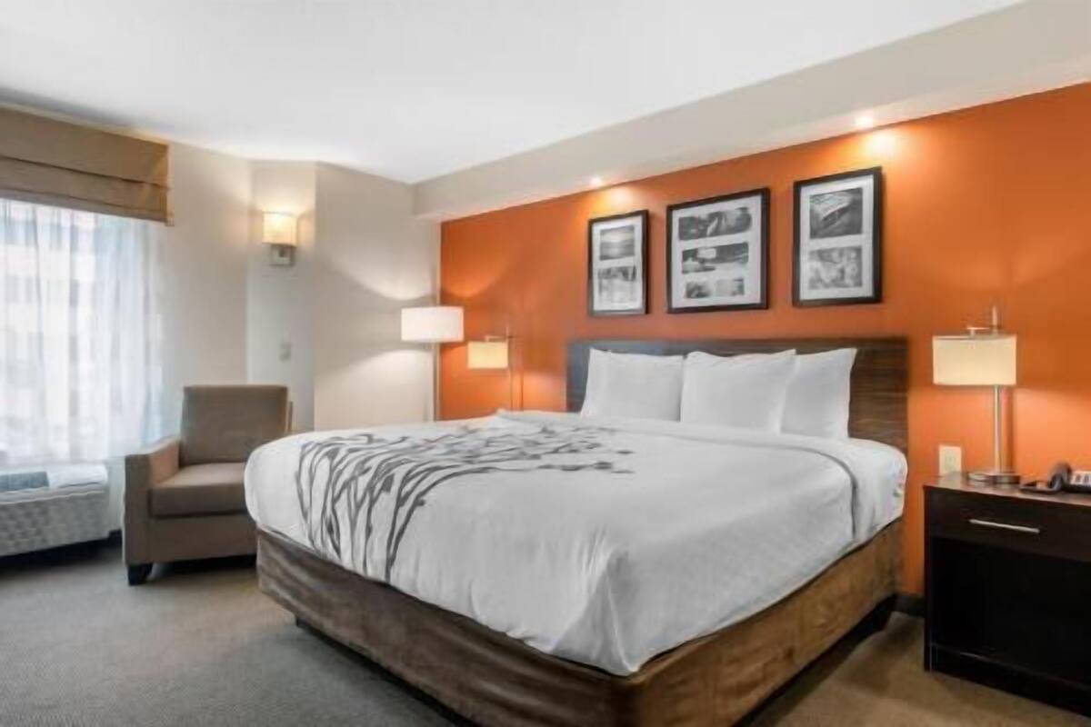 A hotel room with a bed, a chair, a desk, and wall-mounted lamps.