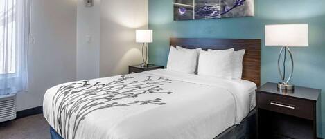 A hotel room with a large bed, two bedside tables with lamps, a wall-mounted artwork, and a window with sheer curtains.