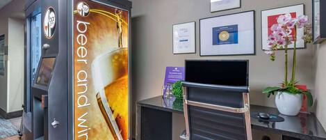 Zona de recepción con dispensador de cerveza y vino, escritorio con computadora, certificados enmarcados en la pared y una orquídea en maceta.