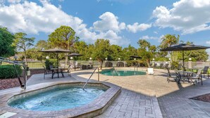 A pool area with hot tub, lounge chairs, and umbrellas.