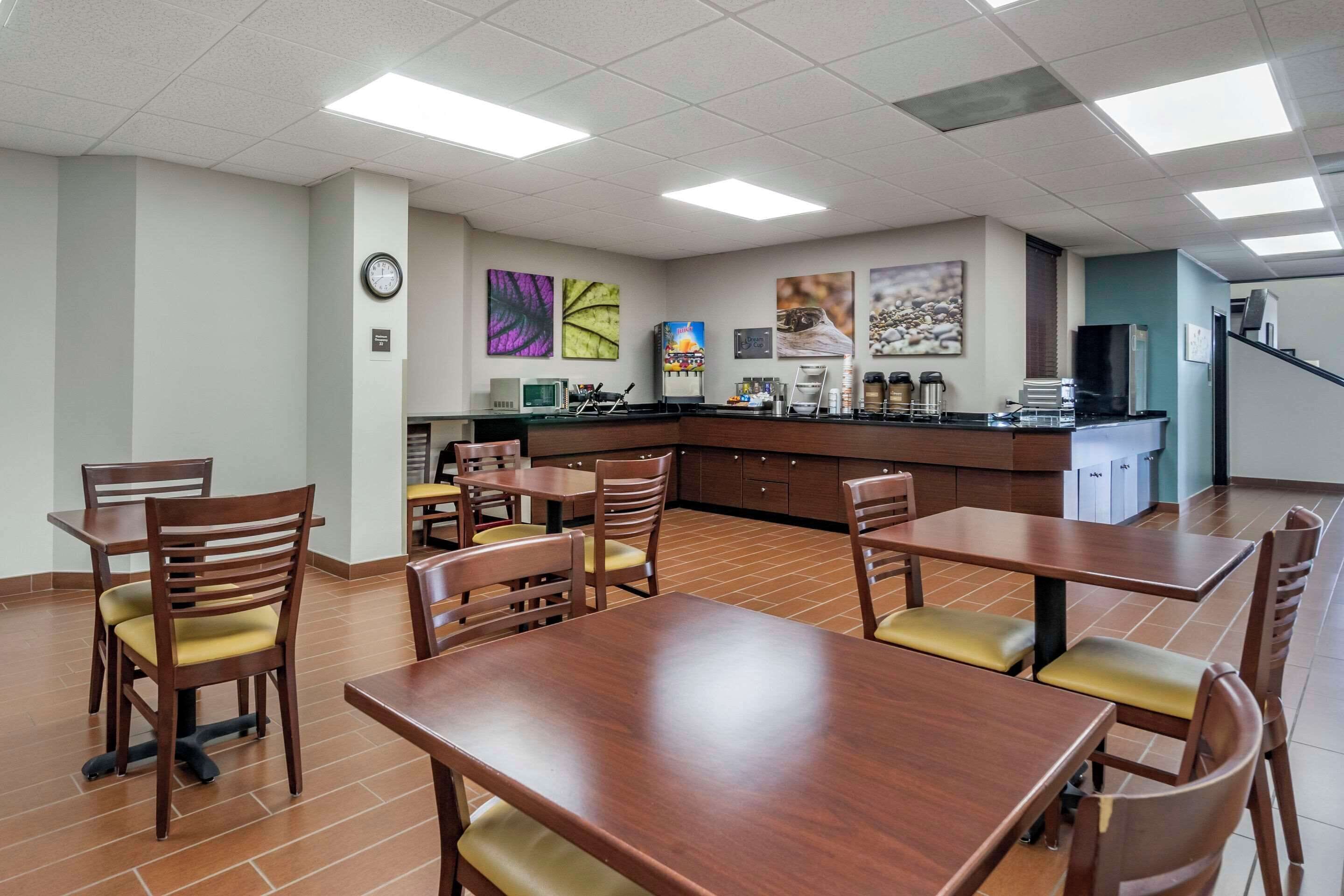A dining area with wooden tables and chairs, a kitchen counter, and artwork on the walls.