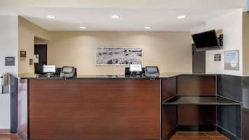 A reception desk with a wooden finish, a digital screen, and a framed picture on the wall.