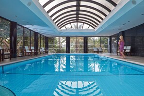 Una piscina techada, una piscina al aire libre, sombrillas