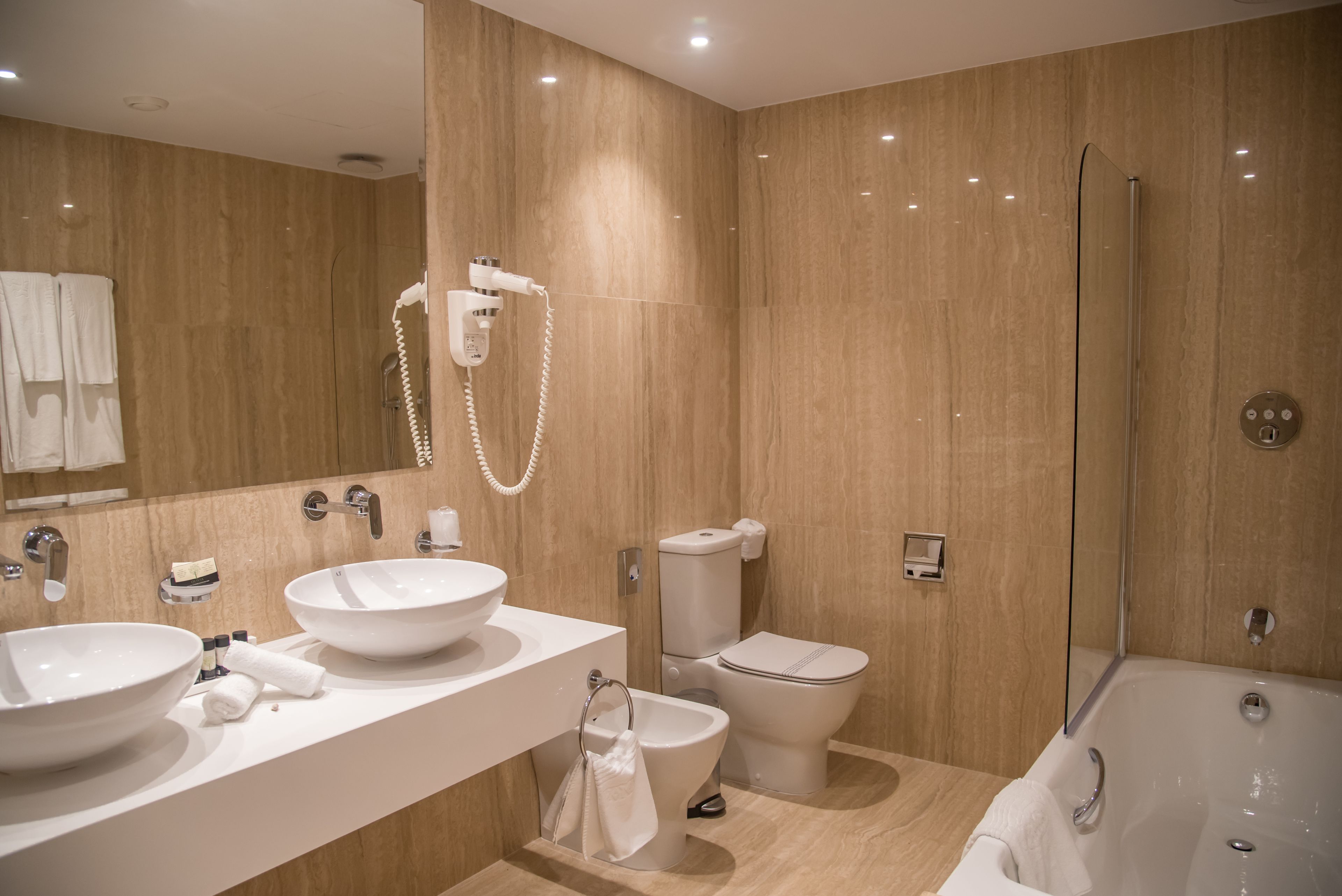 A modern bathroom with two sinks, a toilet, a bidet, and a walk-in shower.
