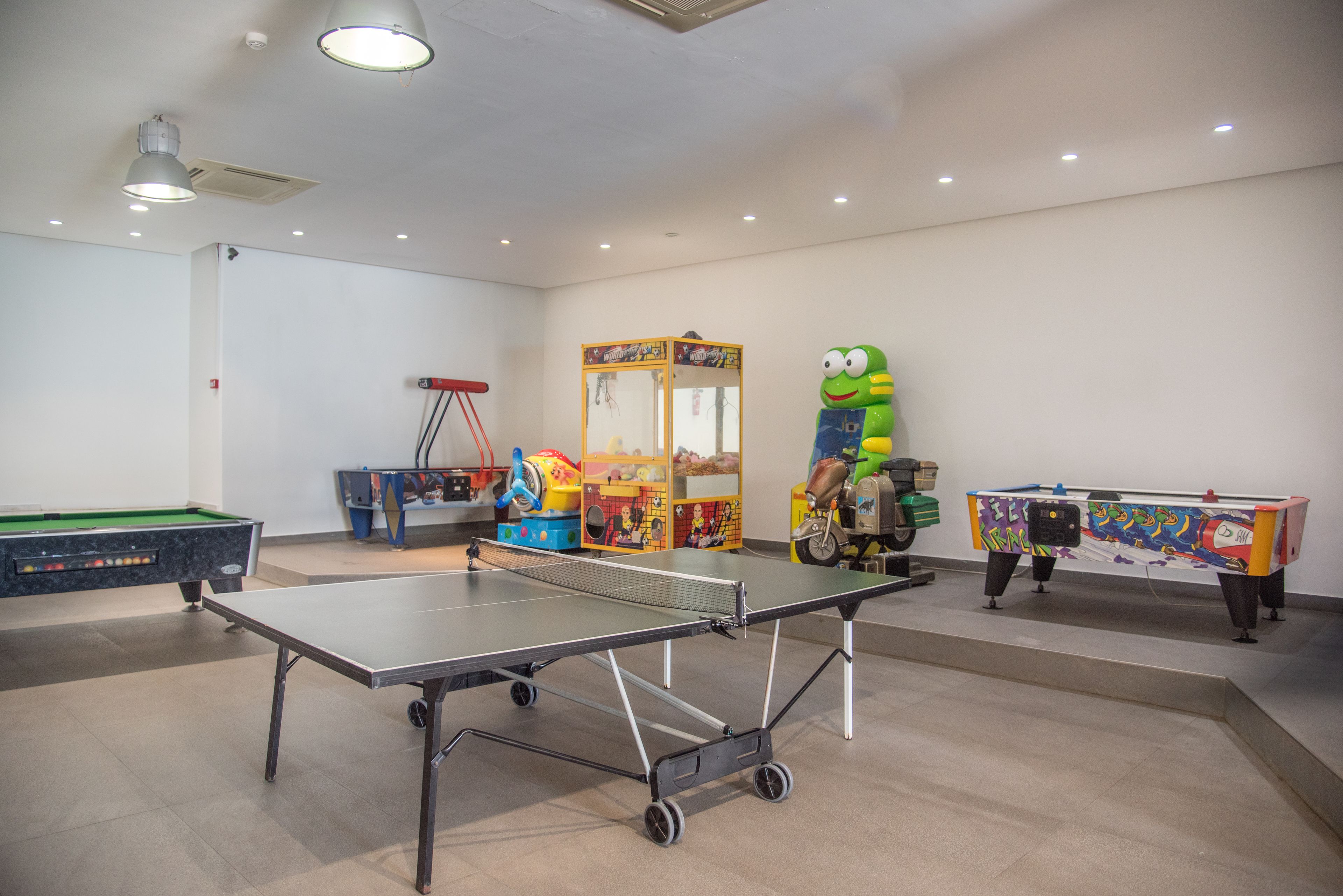 A recreational room with a ping pong table, a pool table, and various children's play equipment.