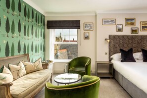 Una habitación con sofá, un sillón verde, una mesa redonda, cama y ventana con vistas a edificios.