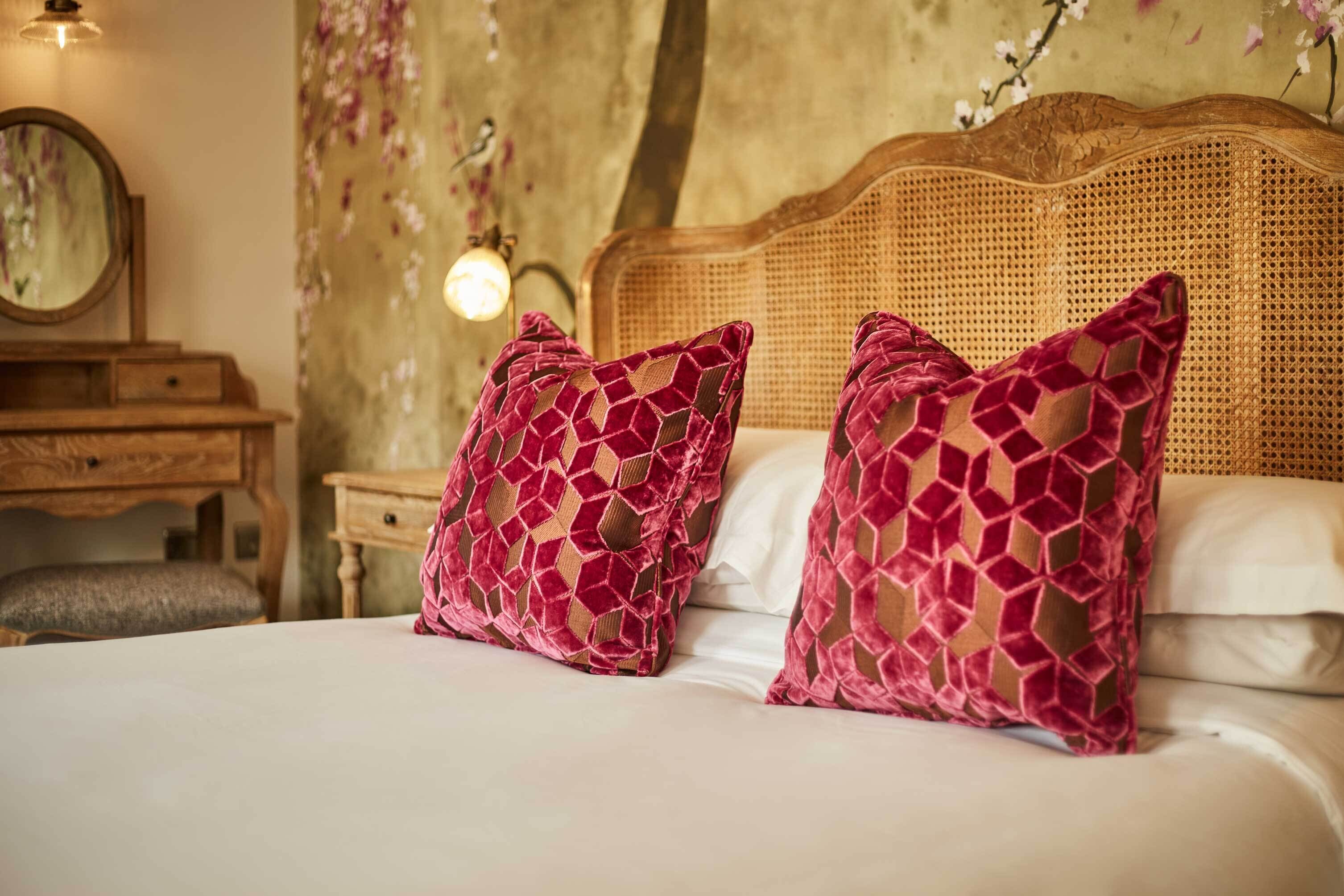 A bed with two patterned pillows, a wooden headboard, a bedside table, and a mirror.