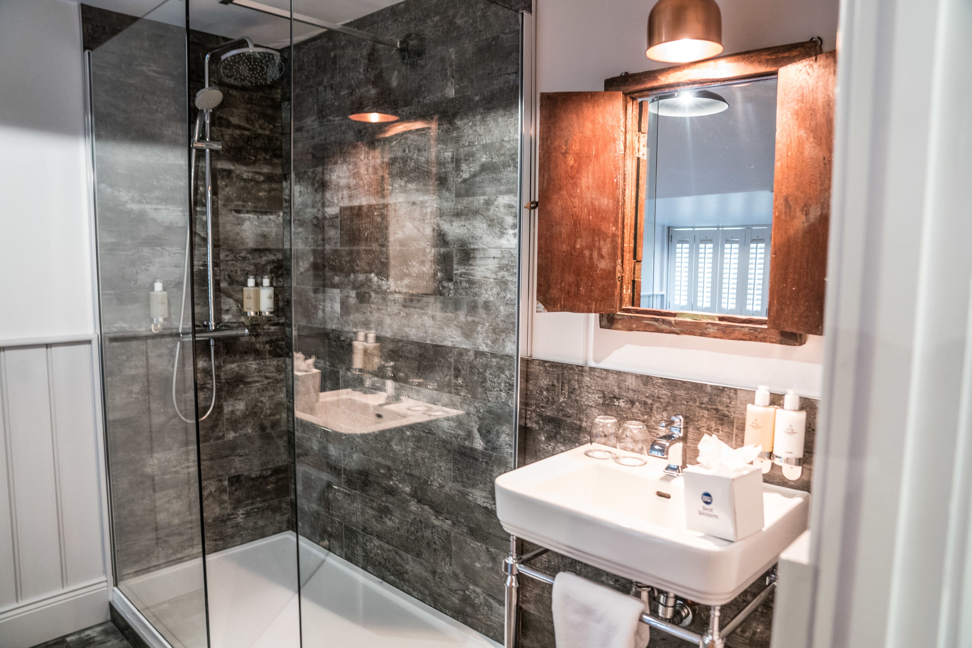 A modern bathroom with a glass-enclosed shower, a white sink with a wooden cabinet above, and a mirror with a wooden frame.