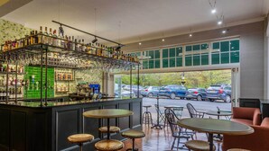 Una zona de bar con taburetes y una barra llena de botellas y vasos.