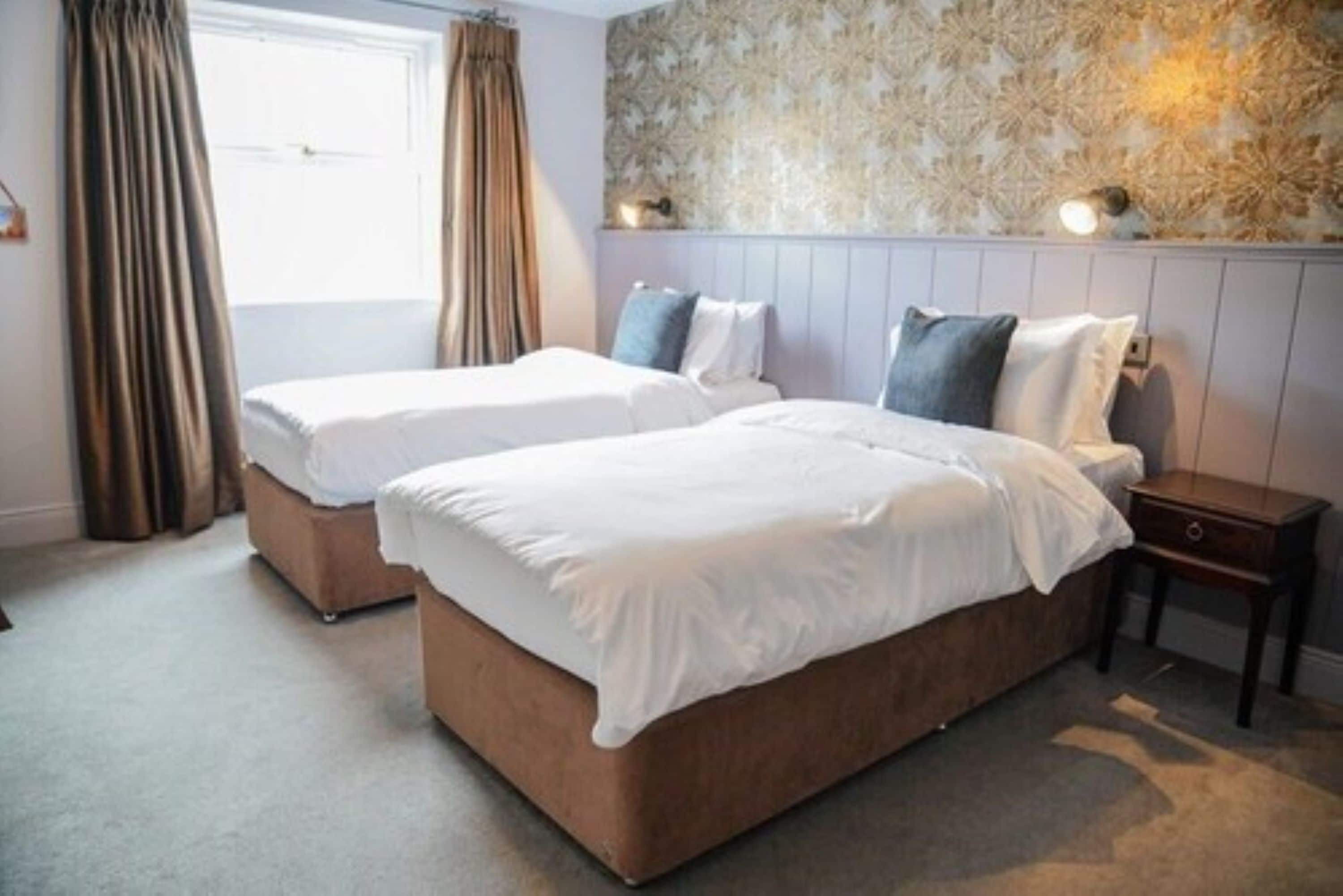 A hotel room with two beds, a nightstand, and a window with curtains.