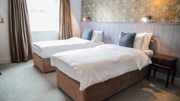 A hotel room with two beds, a nightstand, and a window with curtains.