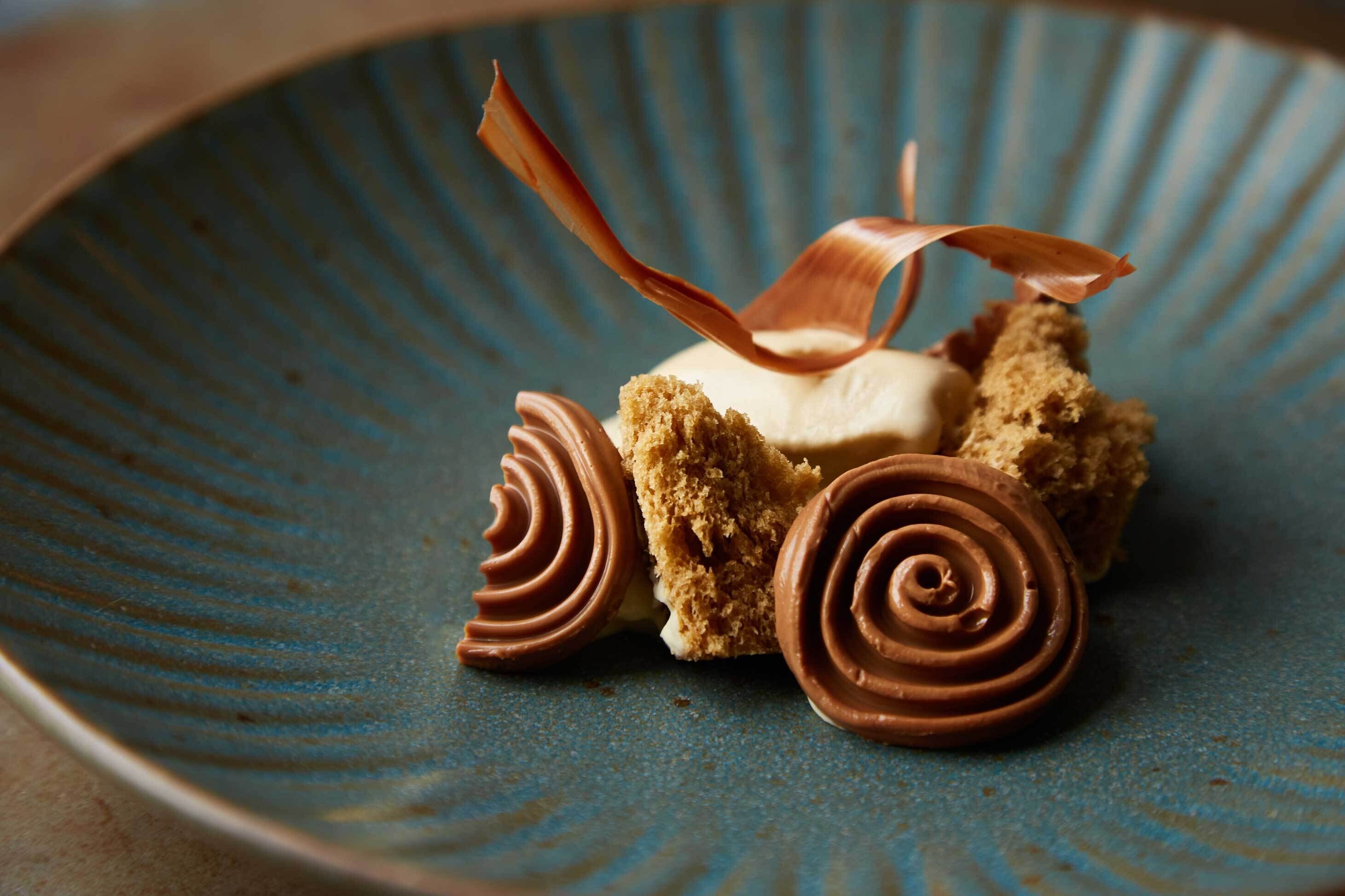 Un postre en un plato azul con remolinos de chocolate y una hoja de chocolate como adorno.