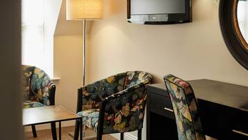 Una habitación con una televisión montada en la pared, un escritorio y dos sillones estampados.