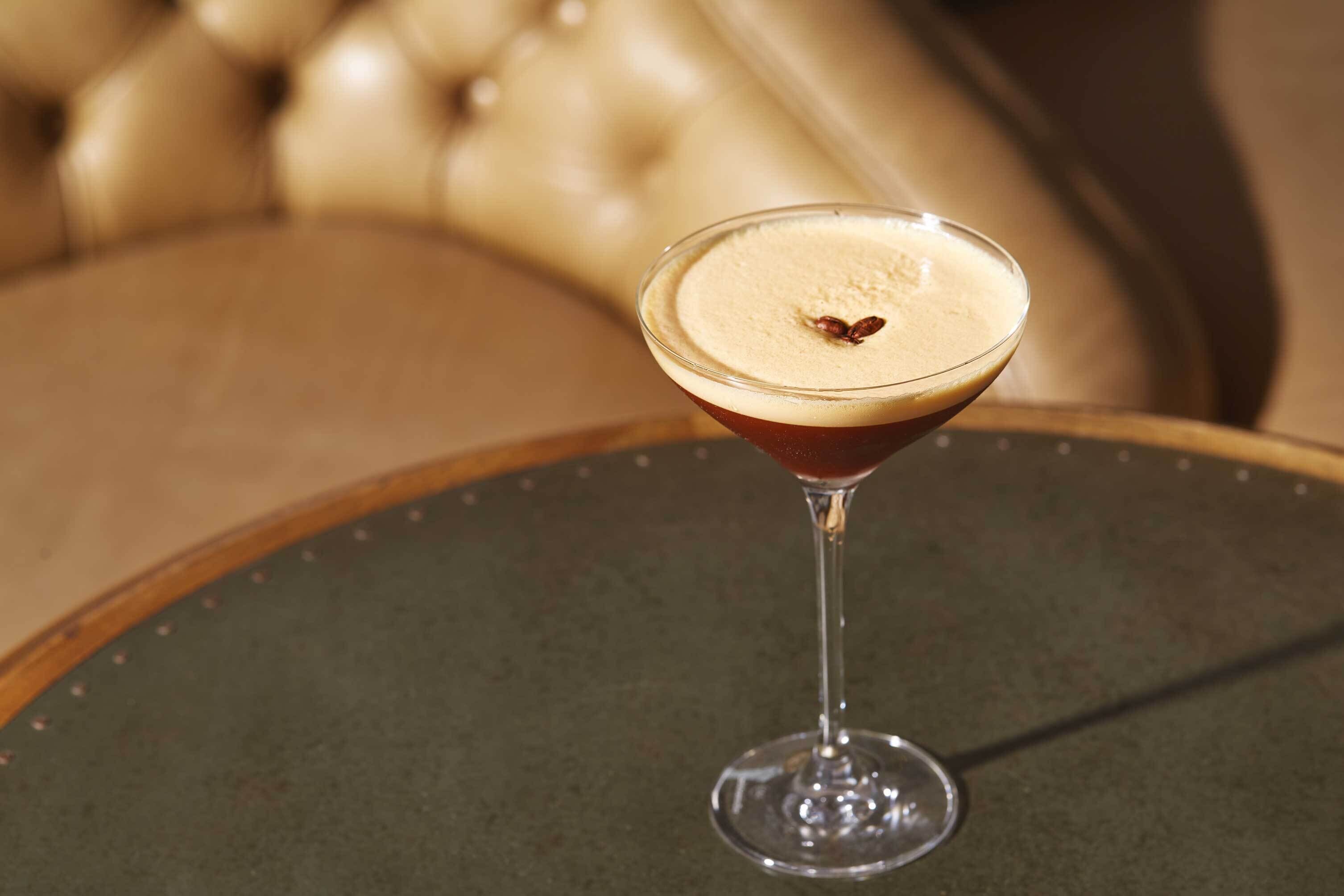 Un verre à martini, surmonté d’une mousse onctueuse, posé sur une table ronde.