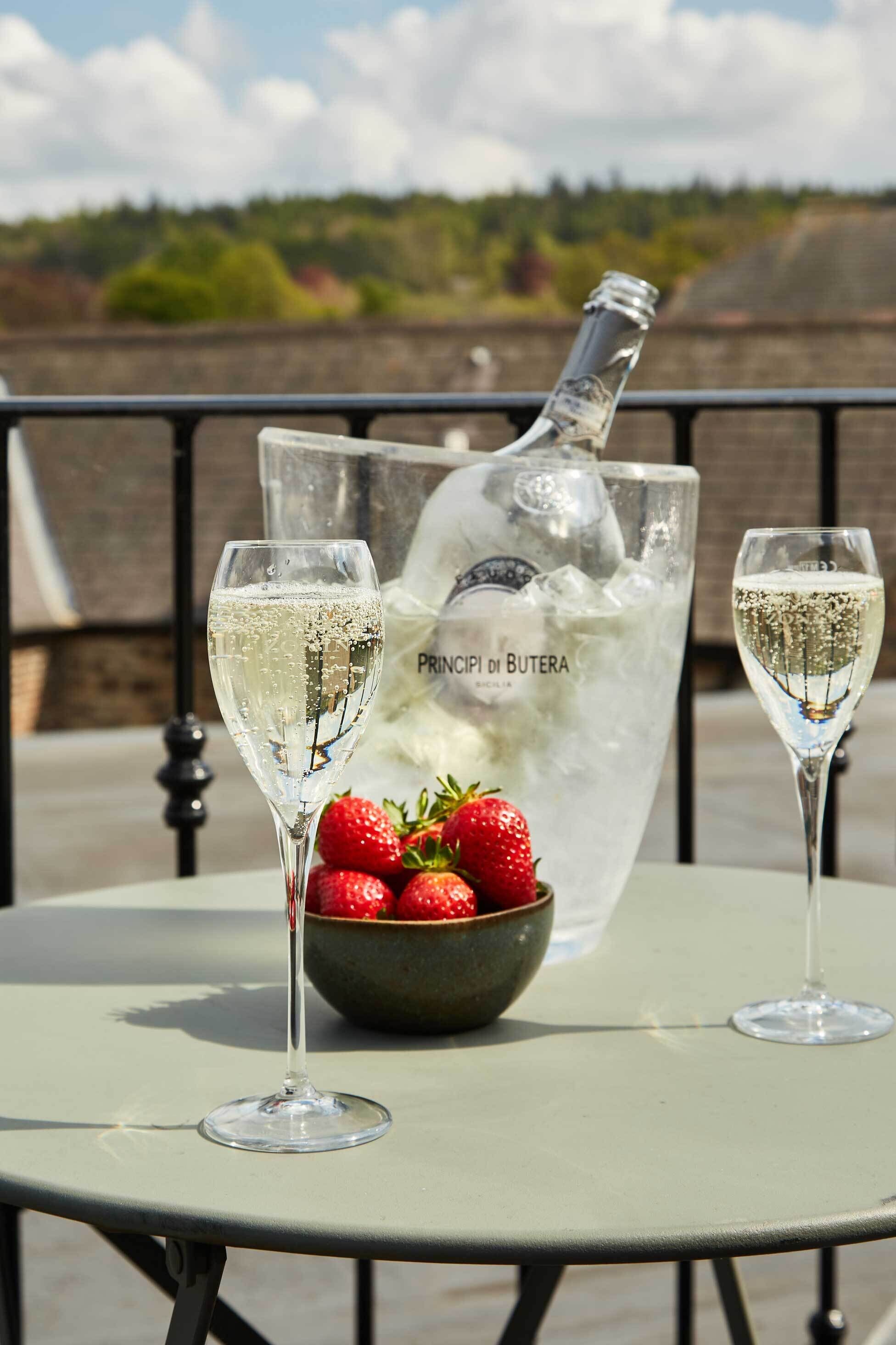 Een tafel met twee champagneglazen, een champagnefles en een schaal aardbeien.