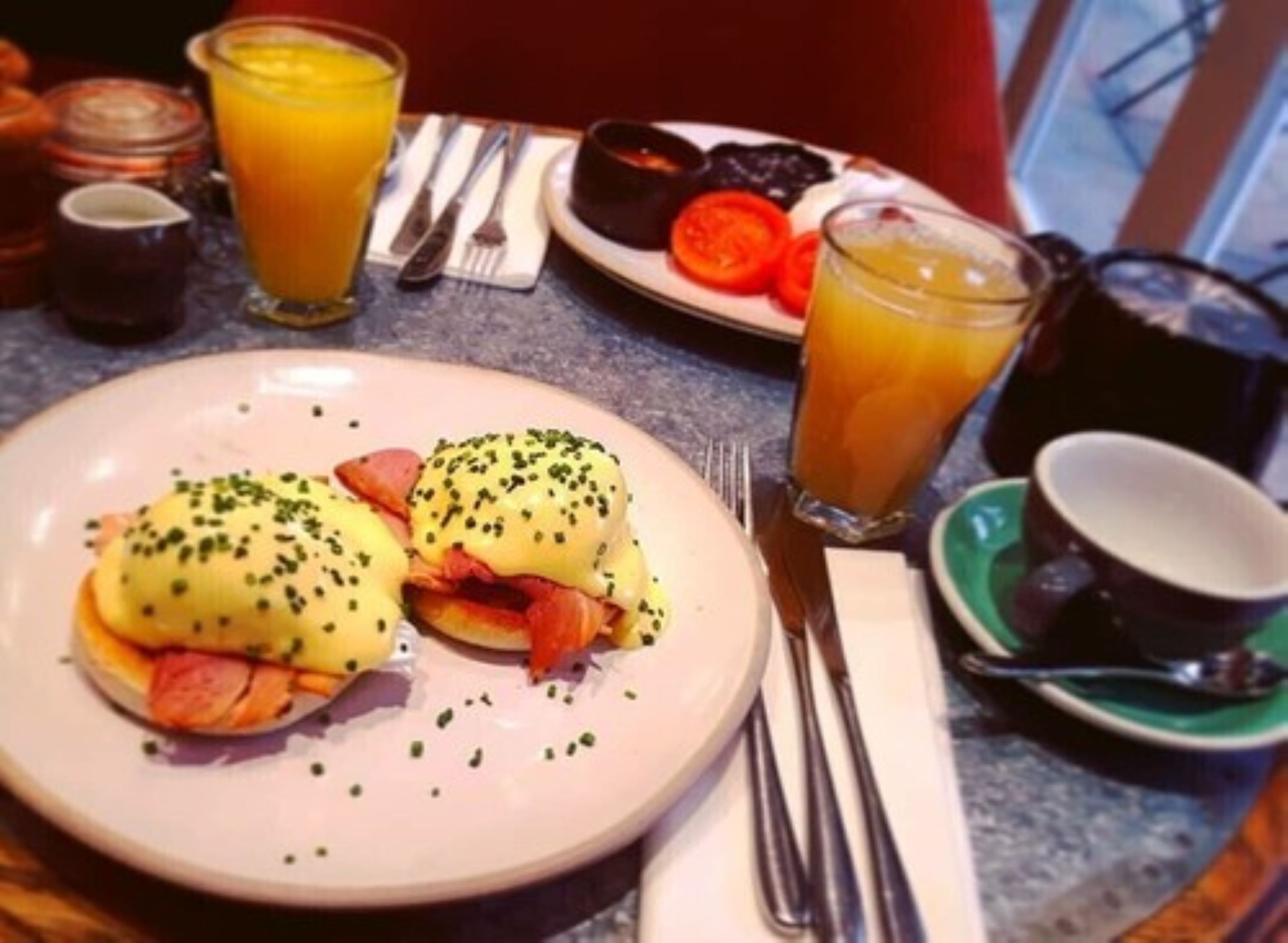 Una mesa con huevos benedictinos, jugo de naranja y una taza de café.