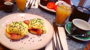 Una mesa con huevos benedictinos, jugo de naranja y una taza de café.