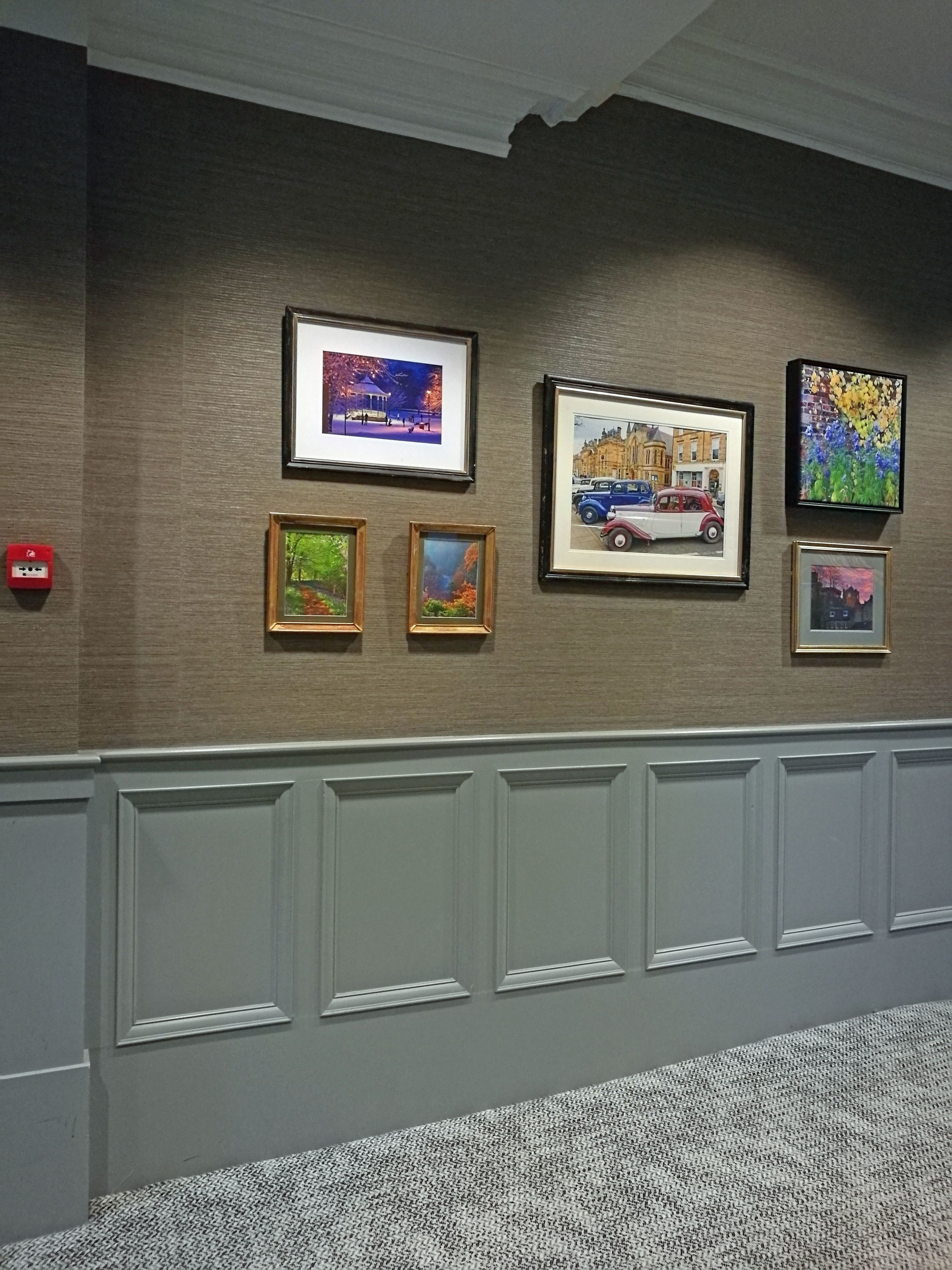 A wall with framed artworks and a fire alarm.