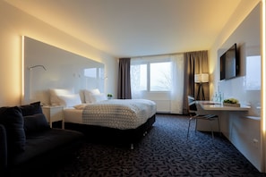 Hotellihuone, jossa on sänky, työpöytä, tuoli, televisio, ikkuna verhoilla ja yöpöytä.