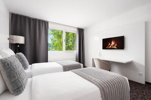 Hotellihuone, jossa on kaksi sänkyä, televisio, takka ja ikkuna, josta avautuu näkymä puita kohden.