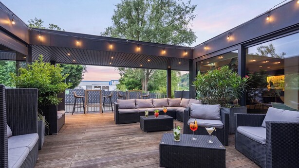 Ein Terrassenbereich im Freien mit Korbmöbeln, einem Holzboden und einer Pergola mit Lichterketten.
