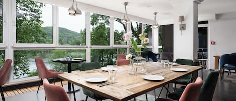 Un comedor con una mesa de madera, sillas y vistas a un lago y colinas.
