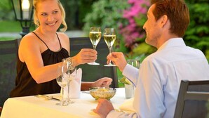 A couple dining outdoors at a table with wine glasses, a bowl of fruit, and a candle. - Hotel Jensen (Lübeck)