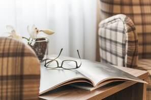A plaid chair, a book, and a pair of glasses on a wooden table. - Hotel Jensen (Lübeck)