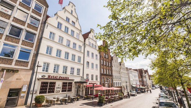 A street with buildings, including a hotel named 'Hotel Jensen' with outdoor seating and a red awning. - Hotel Jensen (Lübeck)