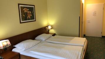 A hotel room with two beds, a nightstand with a lamp, a framed picture on the wall, and a door with a light switch.